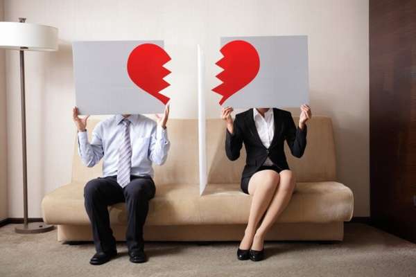мужчина и женщина сидят на диване и держат таблички с половинками сердец 
