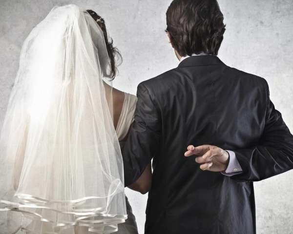 невеста в белом платье и жених в костюме перекрестил пальца за спиной