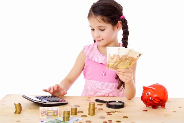 девочка держит деньги в руке и считает на калькуляторе, деньги, копилка и лупа на столе