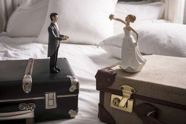 статуэтки жениха и невесты на разных чемоданах на кровати