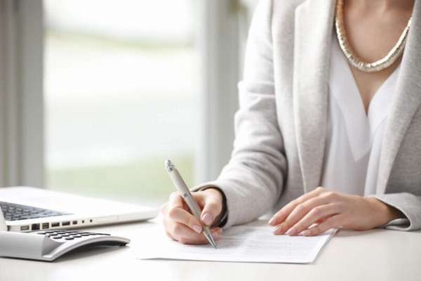 женщина заполняет документы ручкой, калькулятор и ноутбук на столе